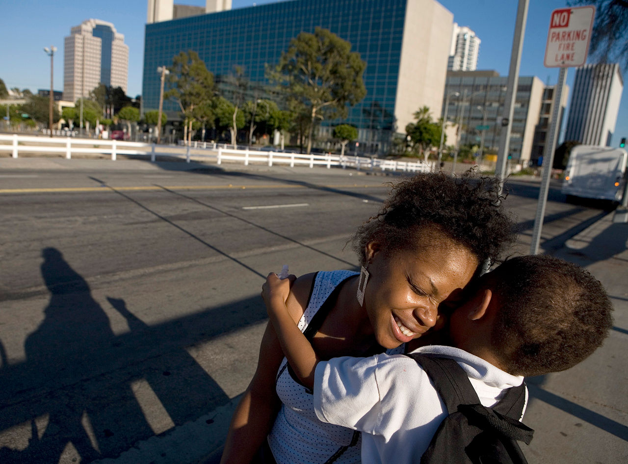 Beverly Davis a single mother hugs her son Semaj as they wait at a bus stop.  Beverly suffers from Crohn's Disease. Commission to Build a Healthier America - Beverly Davis. Long Beach, California.