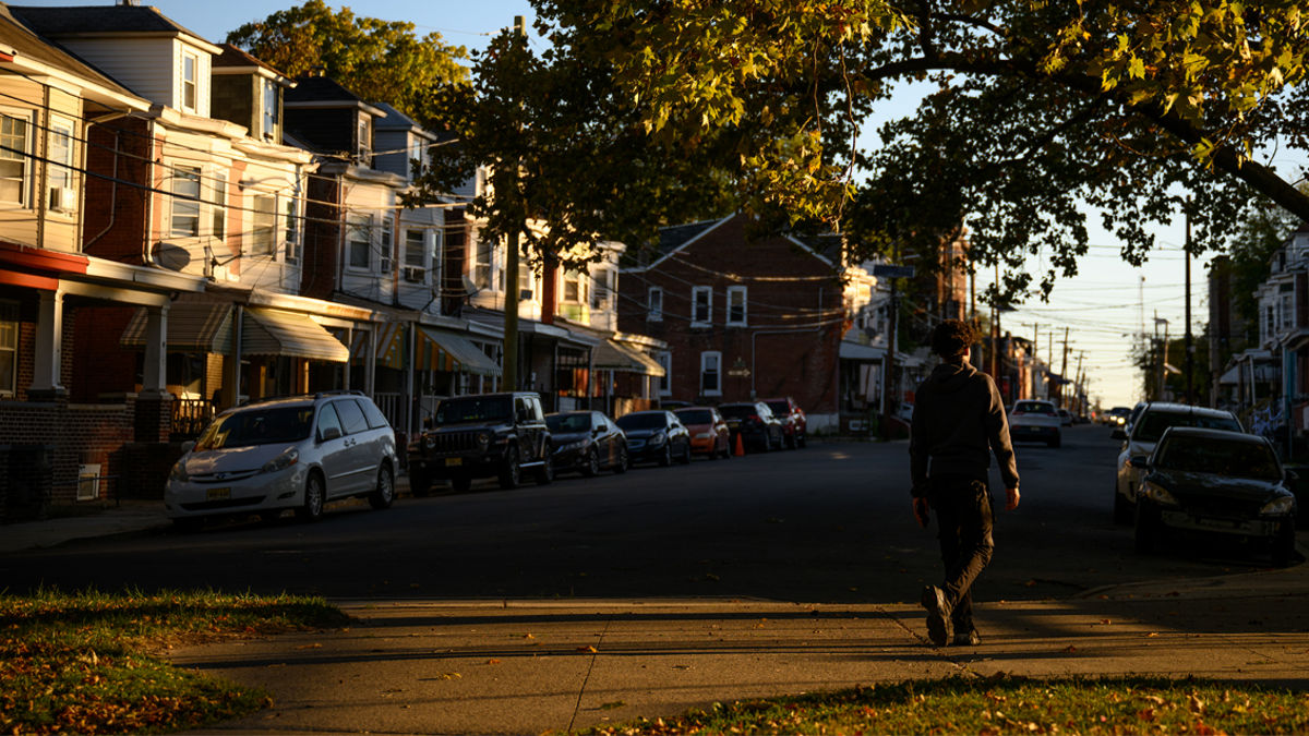 A teen walking across a street toward a sidewalk.