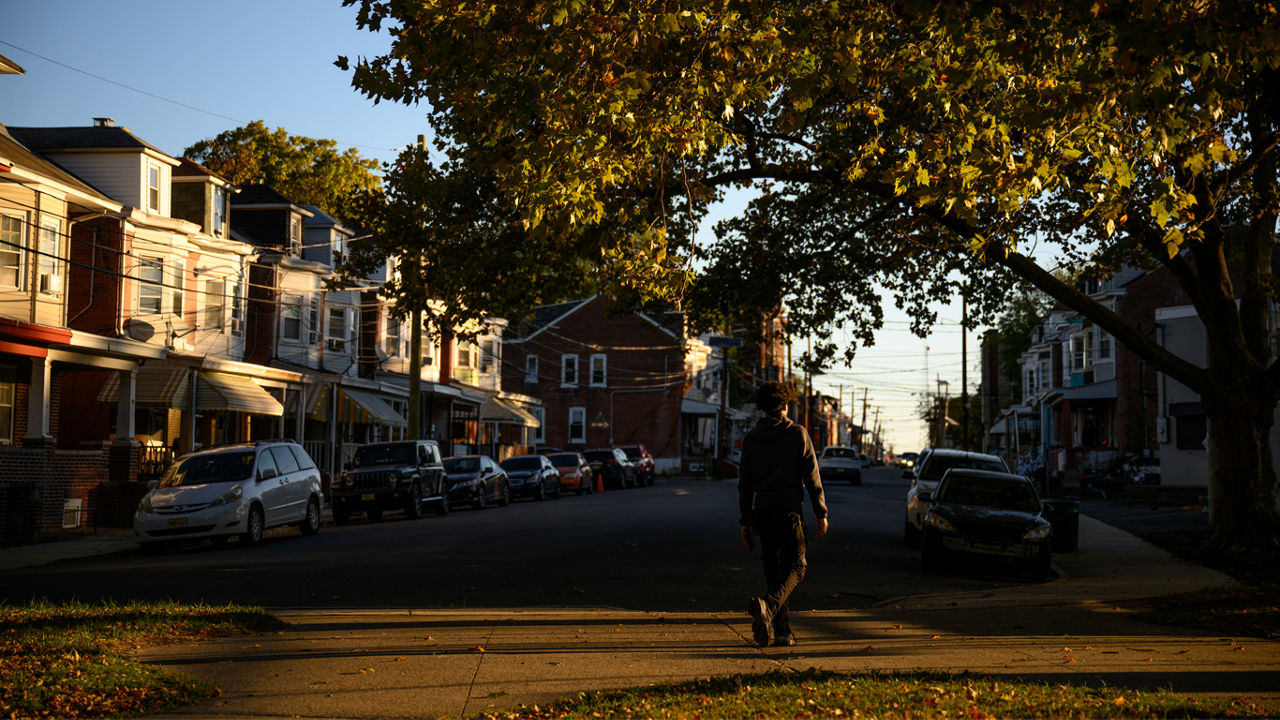 A teen walking across a street toward a sidewalk.