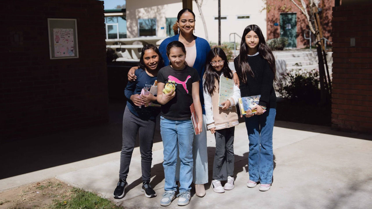 A school principal poses for a photograph with four students outside the school.