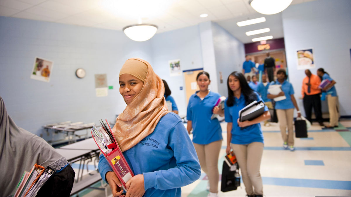 Caring Across Communities is a national program supporting mental health services in schools.  Remale refugee students walking in school carrying books.