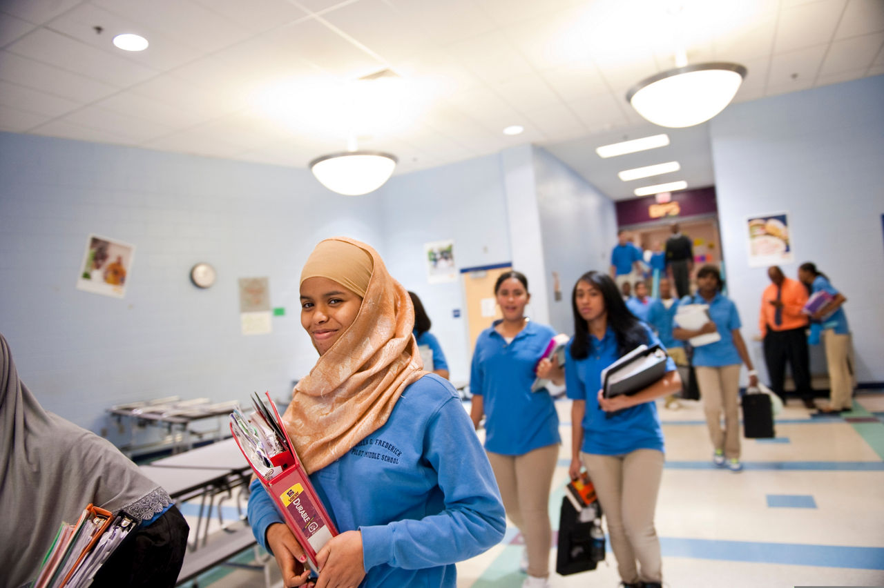 Caring Across Communities is a national program supporting mental health services in schools.  Remale refugee students walking in school carrying books.