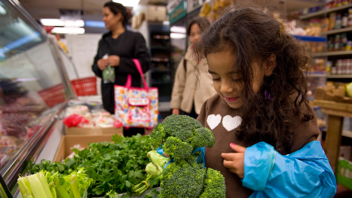 A girl looking at broccoli in a store.