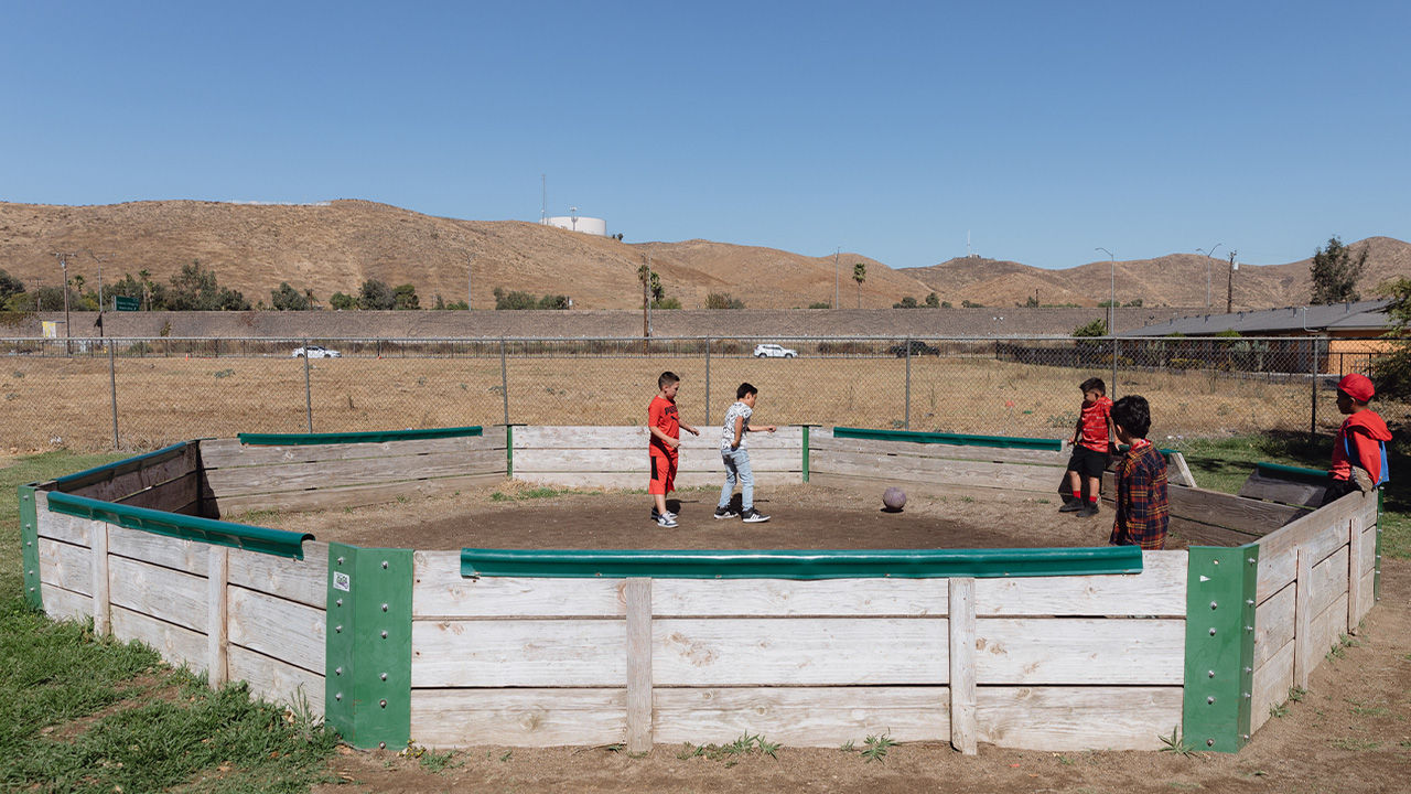 A group of boys in rural America play with a ball inside a corral. 