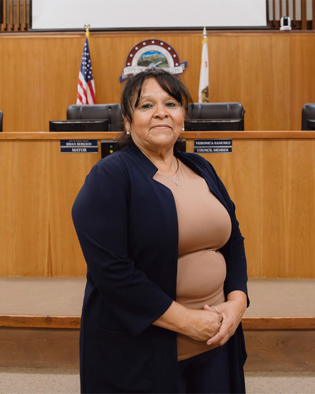 A woman poses for a photograph in front of a desk where city executives make policies. 