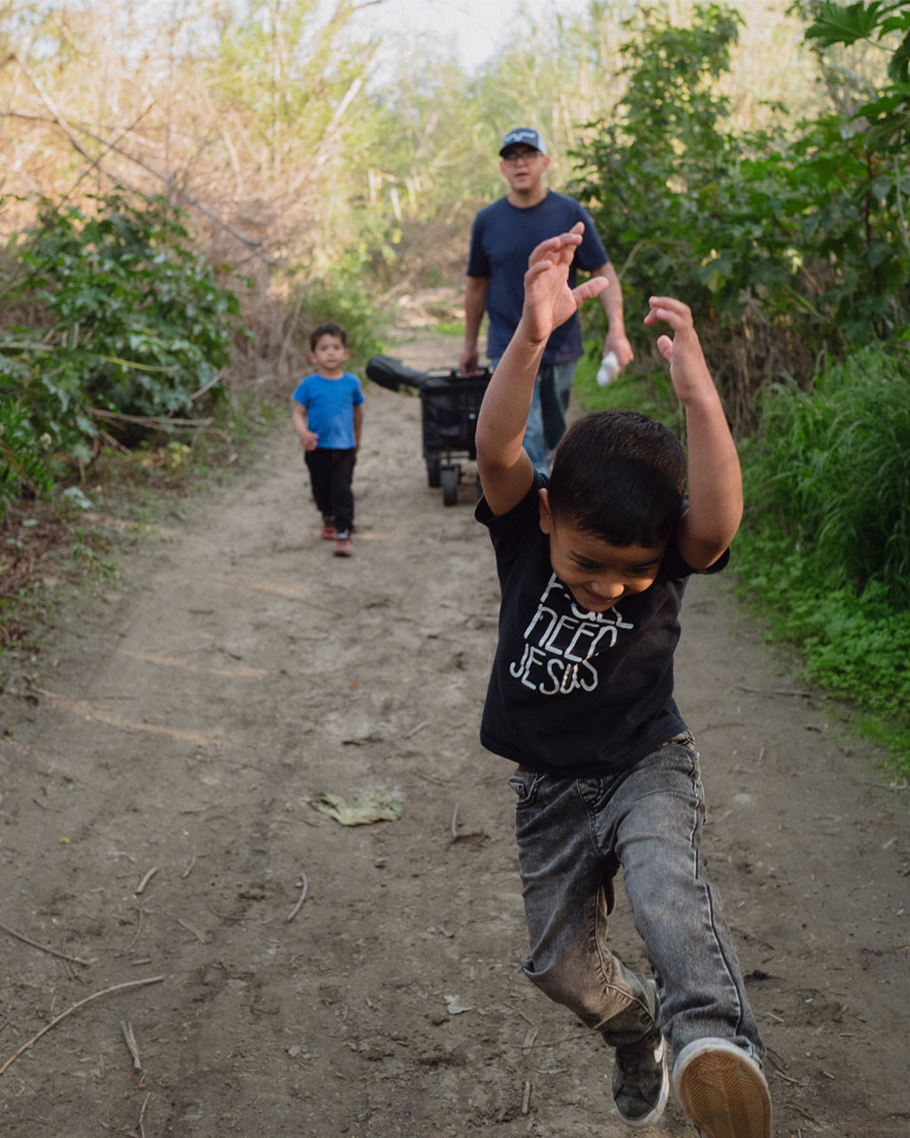 A man and his two young sons walk down a rural road after an evening playing in the river. 