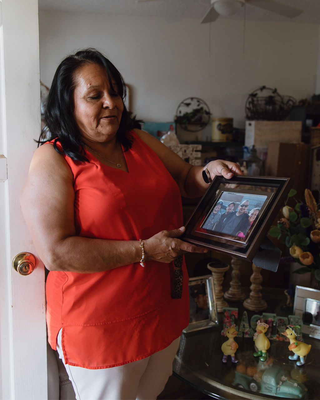 A woman wearing a red sleeveless shirt holds up a framed photograph of her family. 