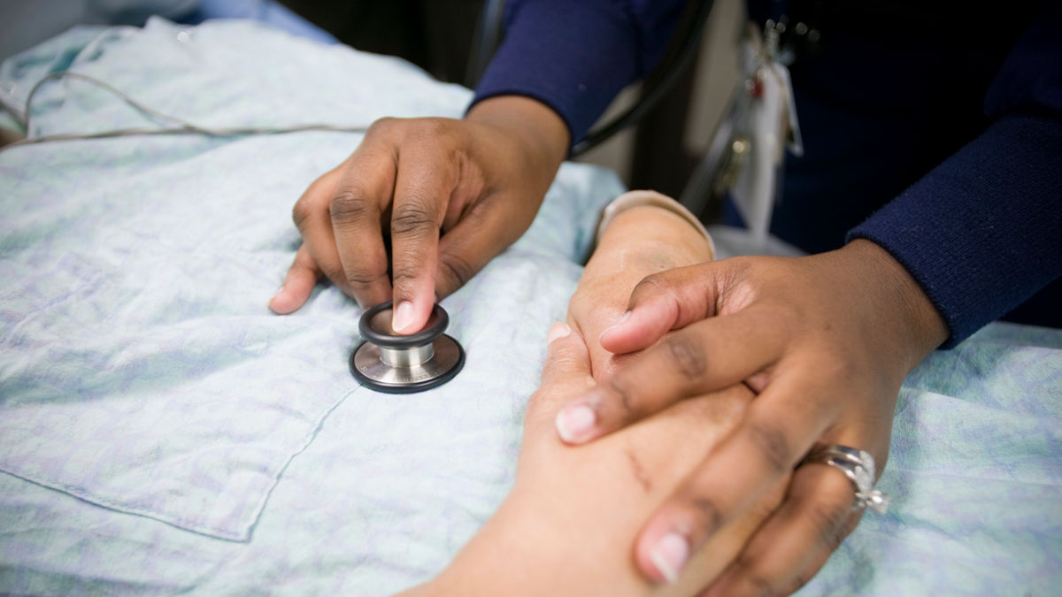 Doctor holds a patient's hand while listening to her heart. 