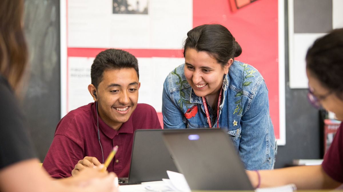 A woman looks over a student's shoulder as he works on a laptop.