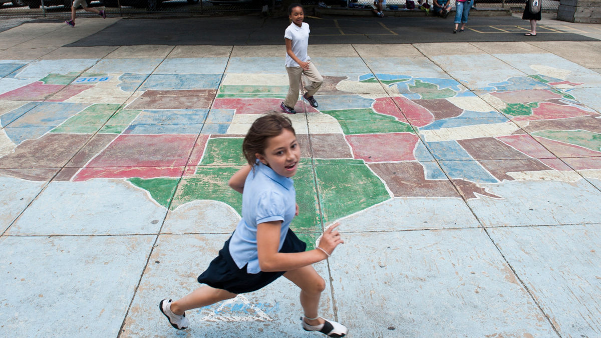 A girl running outside near a chalk drawing of the continental United States.