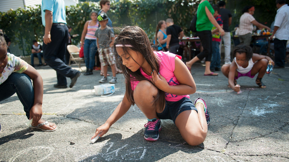 A young girl enjoys drawing on the pavement with chalk.