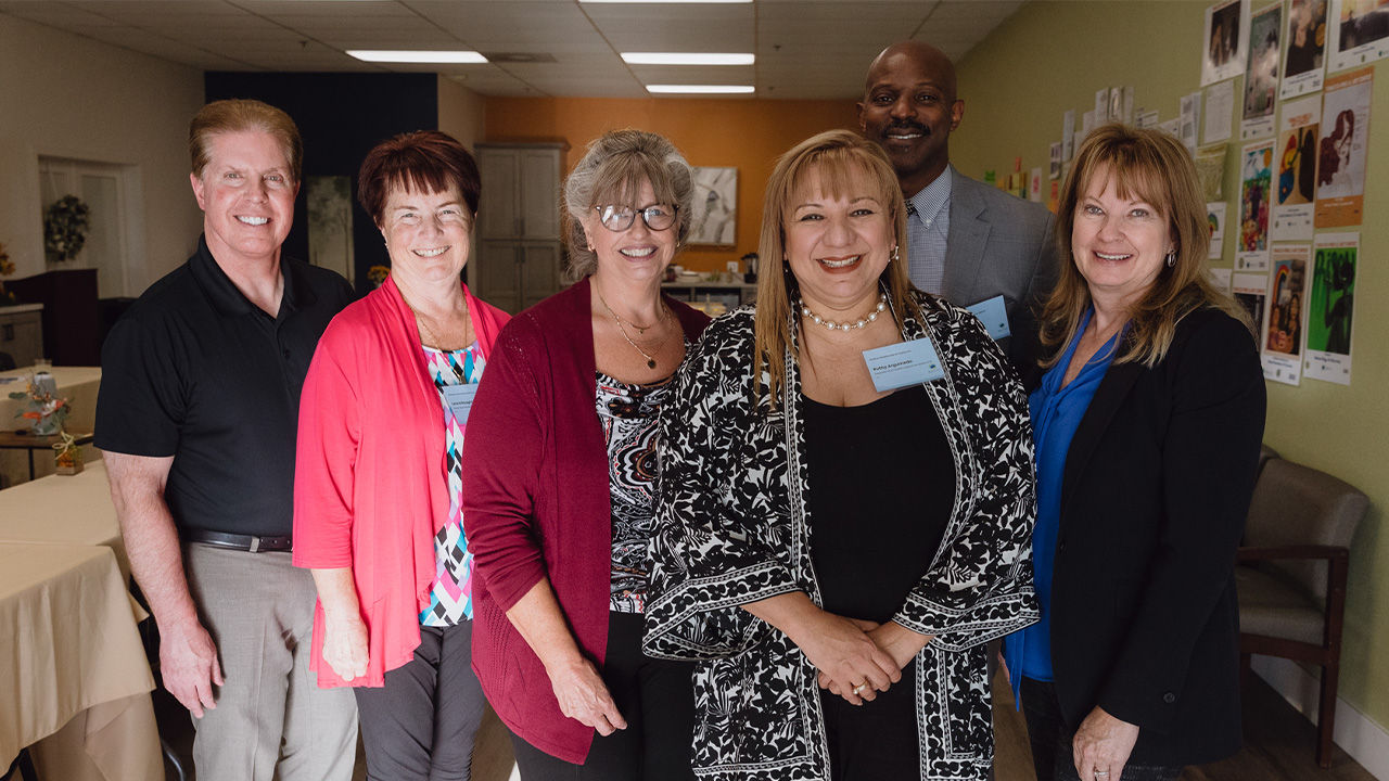 A group of six people wearing nametags posing for a photograph inside a community center. 