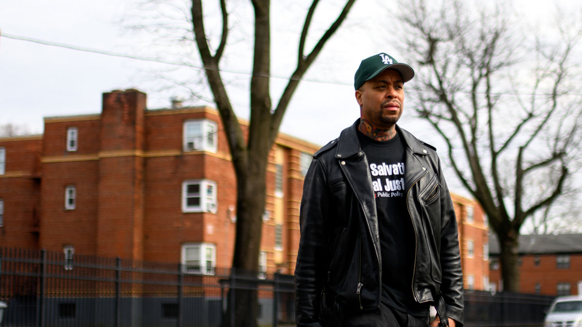 A man walking across a street with brick buildings in the background.