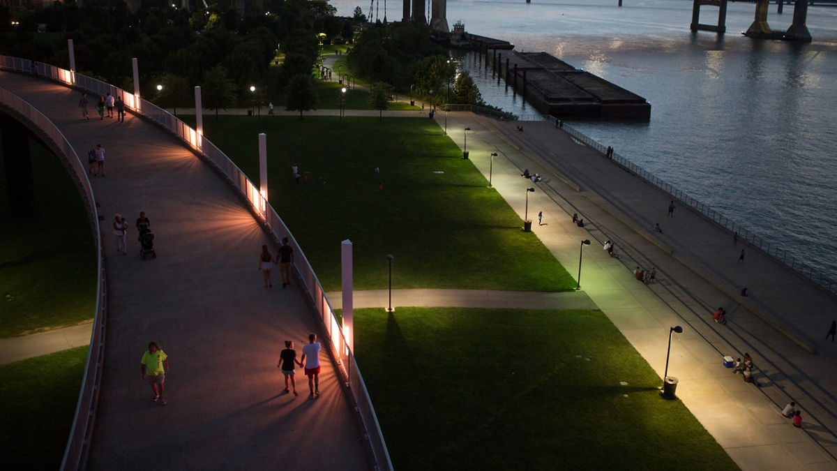 A well-lit pedistrian path beside a bridged river.