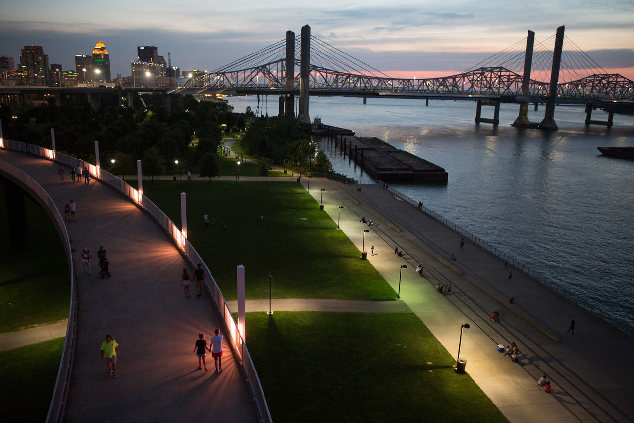 A well-lit pedistrian path beside a bridged river.