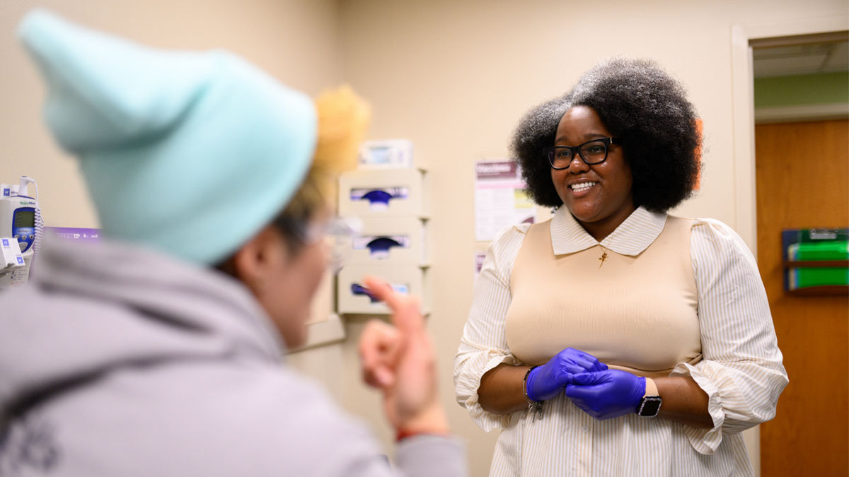 A staff member at a medical center demonstrating a patient exam. of a woman in a knit cap.
