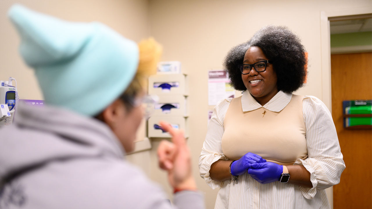 A staff member at a medical center demonstrating a patient exam. of a woman in a knit cap.