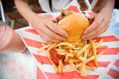 Hands of woman holding hamburger, with fries and ketchup. A strawberry milkshake is on the side.