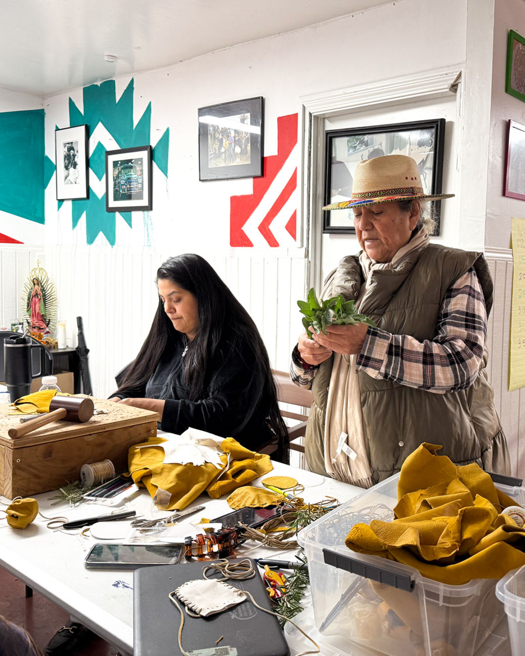 Two people, one wearing a hat, making medicine bags.