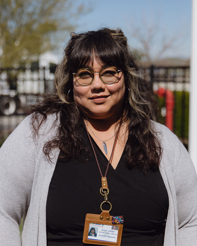 A portrait of a community leader standing outside in the sunlight, wearing a name badge.