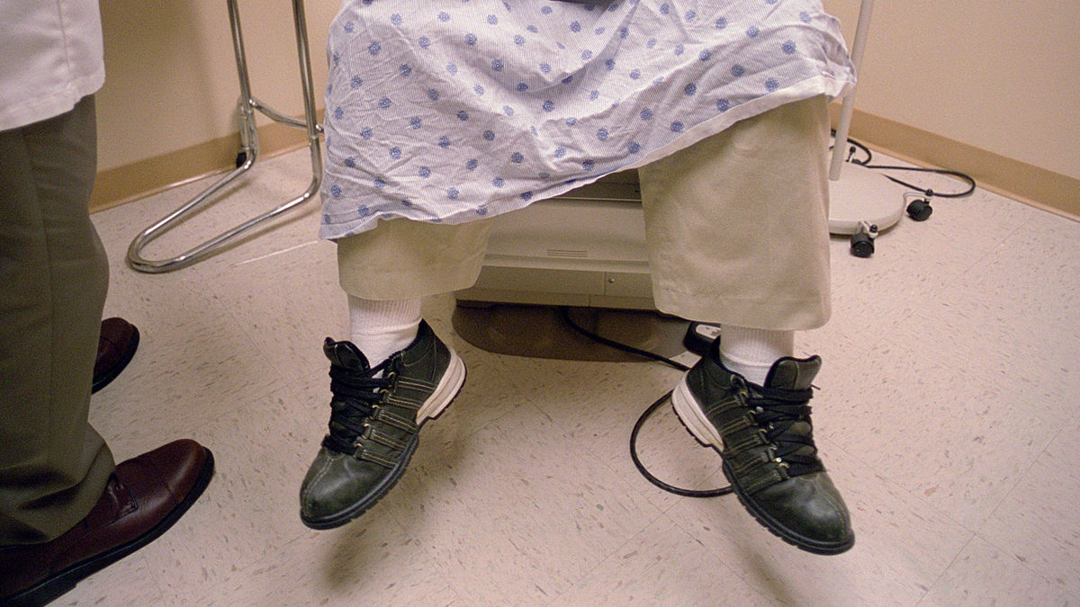 A man sitting on an examining table in a doctor's office searing sneakers.