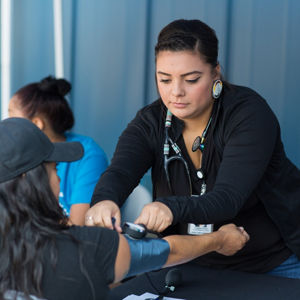 A nurse takes the blood pressure of a woman at a table.