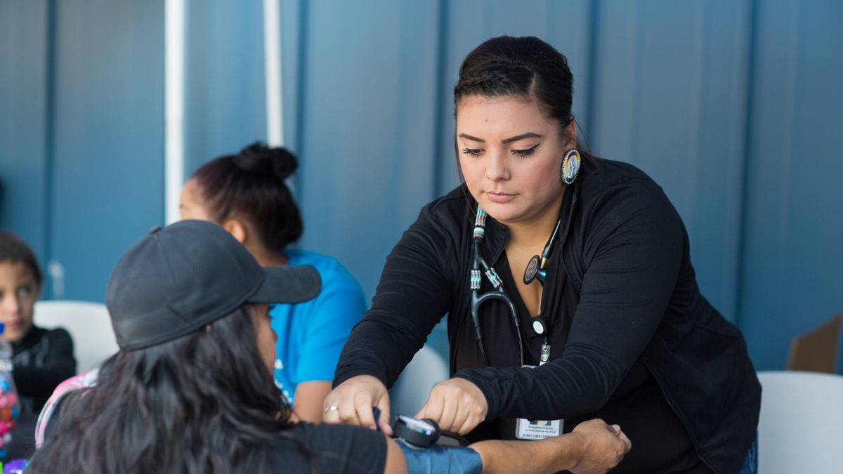 A nurse takes the blood pressure of a woman at a table.