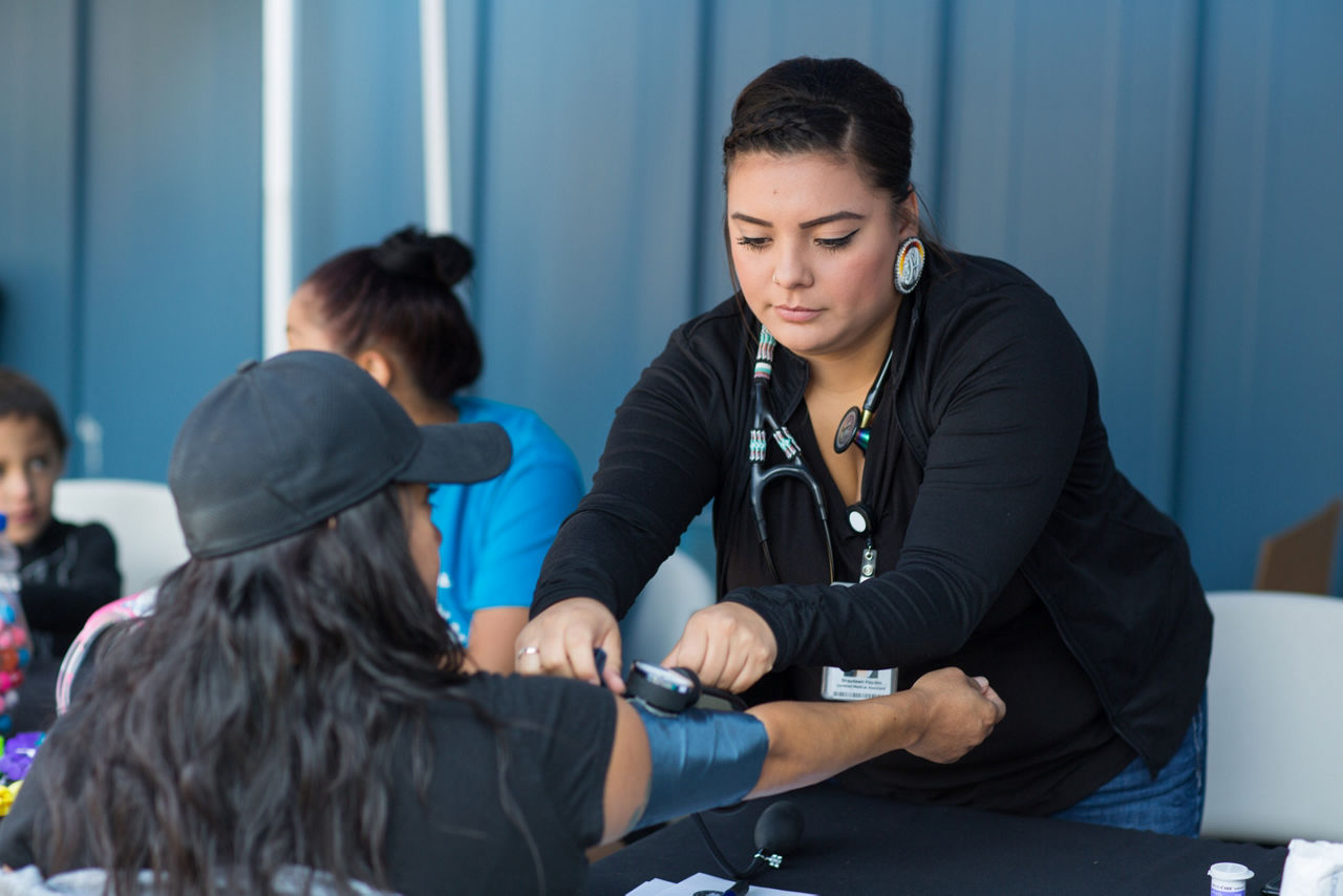 A nurse takes the blood pressure of a woman at a table.