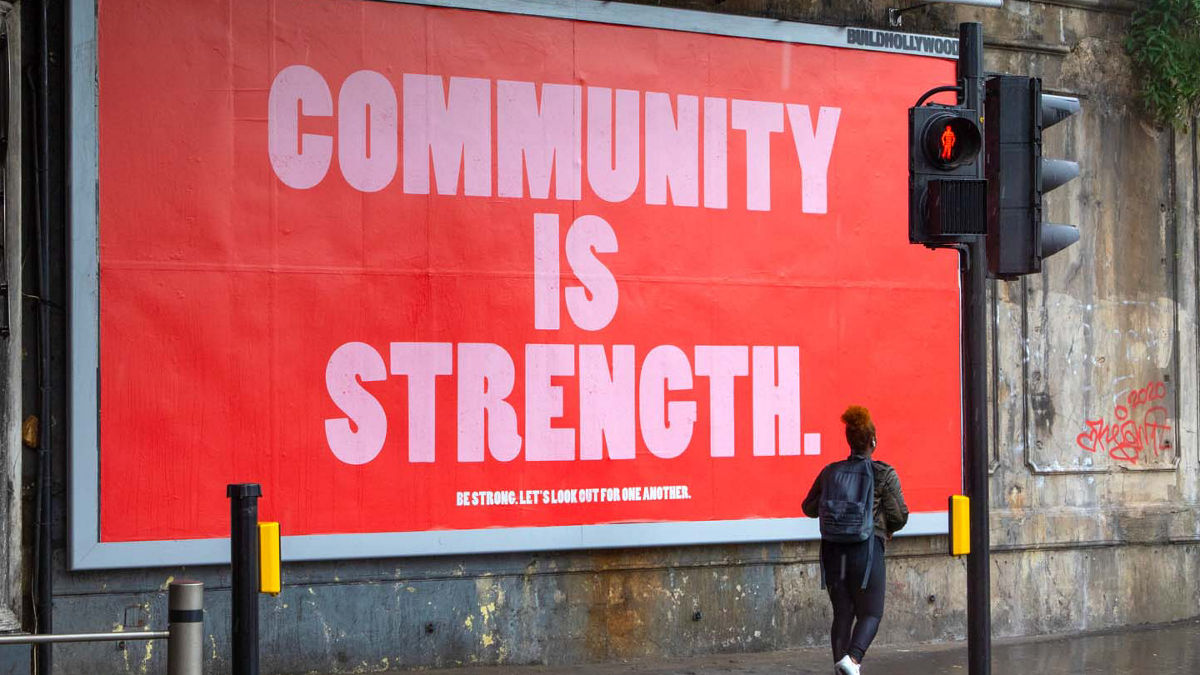 A billboard with the message "Community is Strength" is on display as a woman walks by. 