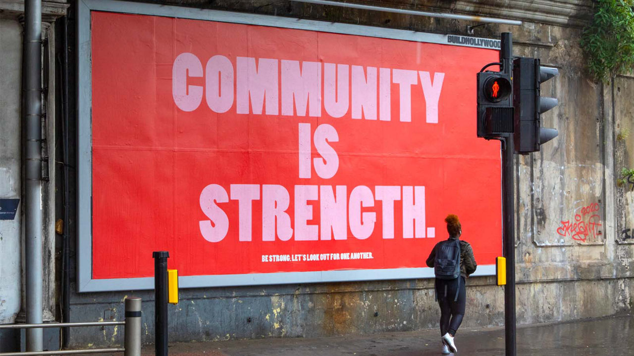 A billboard with the message "Community is Strength" is on display as a woman walks by. 