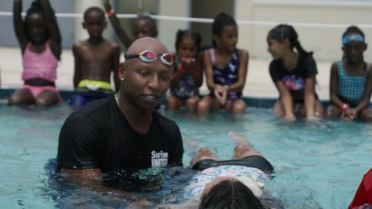 Cullen Jones holding a child while they float on their back in a pool.