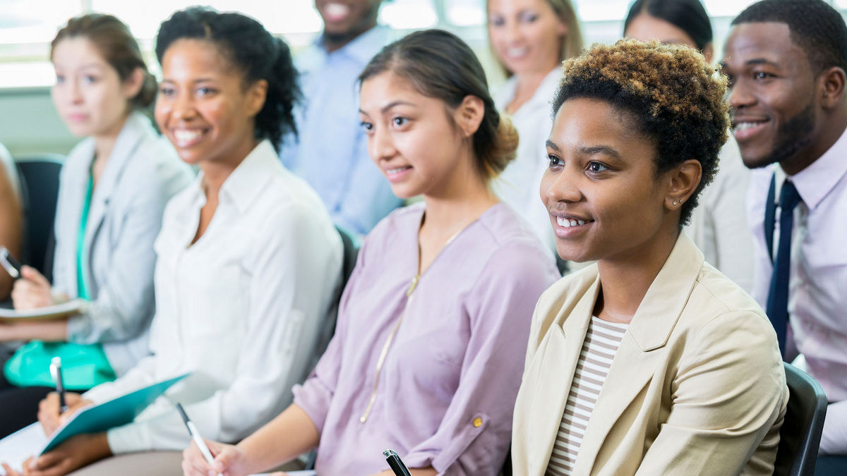 Diverse group of businesspeople listen to conference speaker.