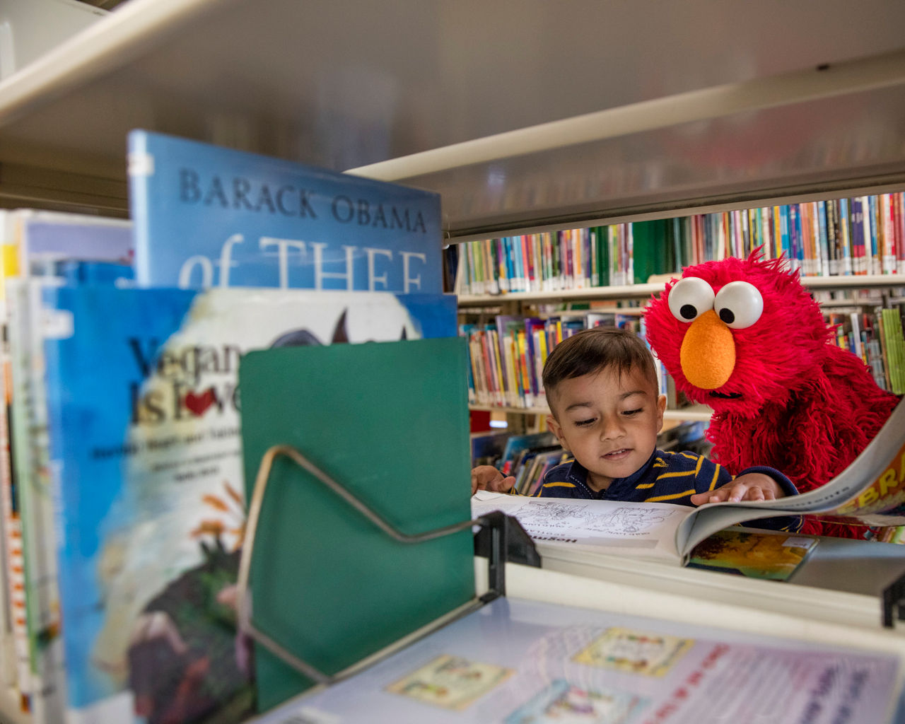 Sesame Street's Elmo and a little boy read together in a library.