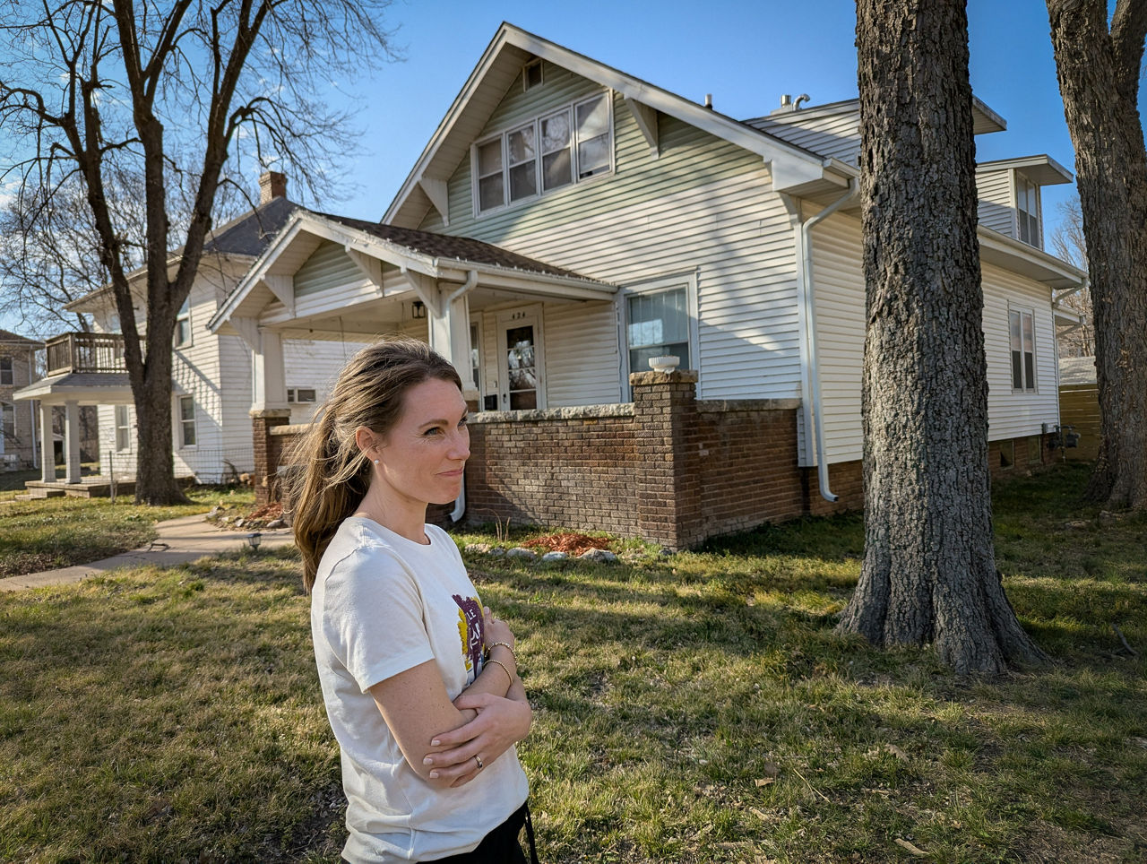 A photo of Emily Bailey in front of a yellow house in Manhattan, Kansas.