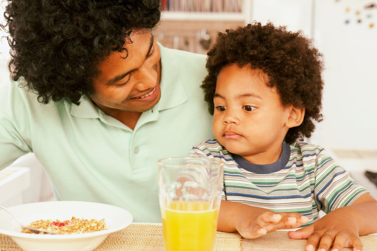 A father and his son eating breakfast cereal and drinking orange juice. Diverse Families.