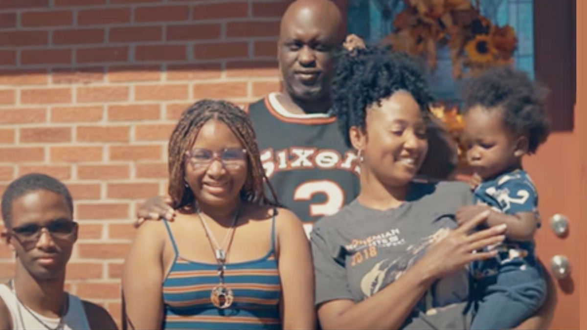 A family of 5 stand in front of their brick home.