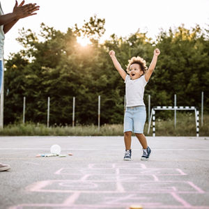 A young child playing hopscotch in a school yard with an adult.