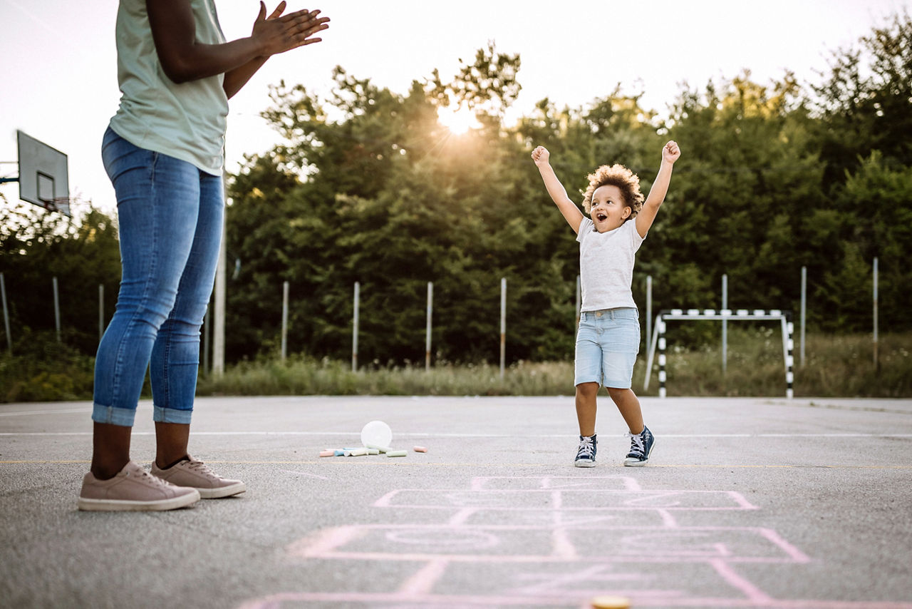 A young child playing hopscotch in a school yard with an adult.