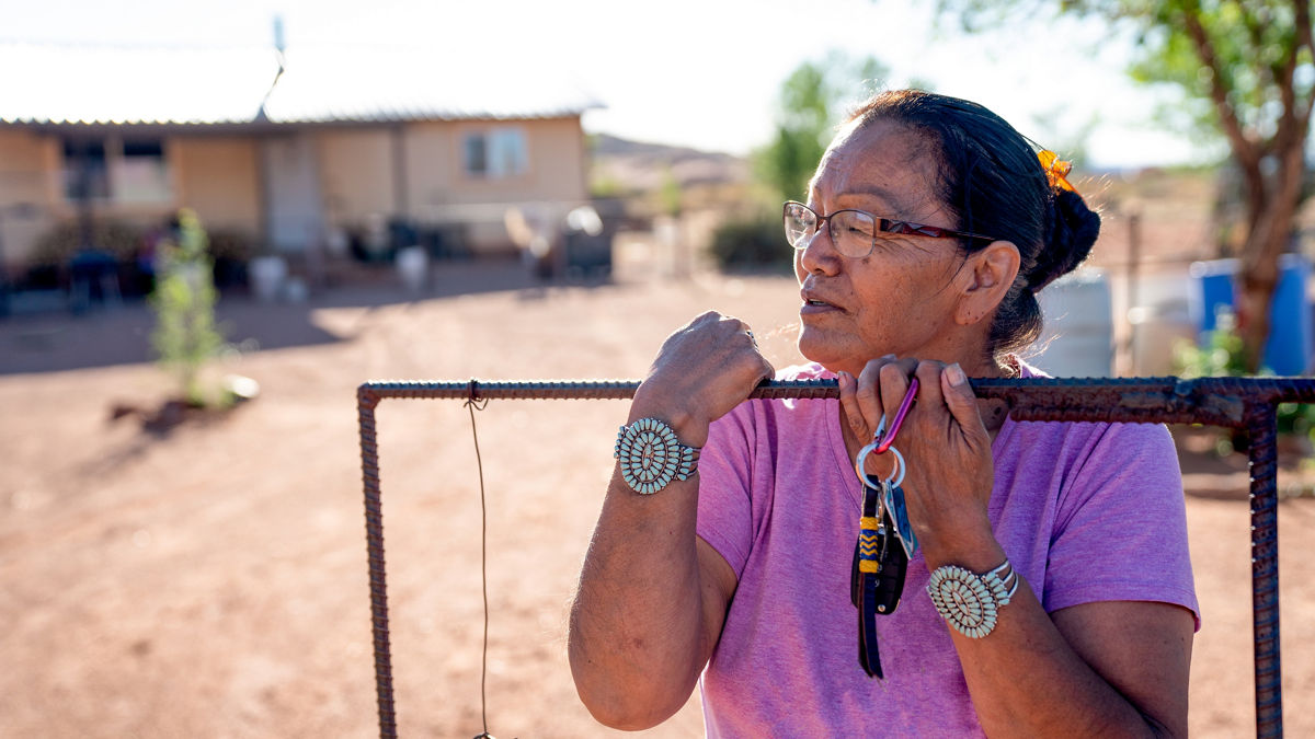 A Navajo woman standing by the gate of her yard.