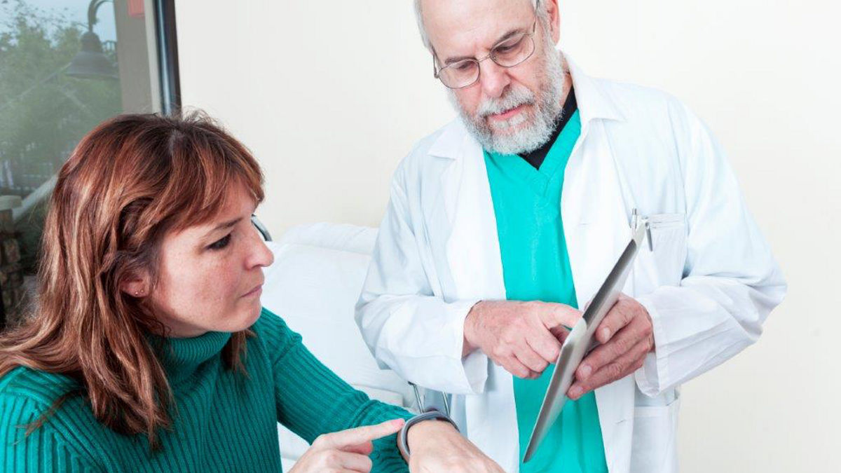 A male medical professional shows woman how to use health monitoring on tablet and smart watch.