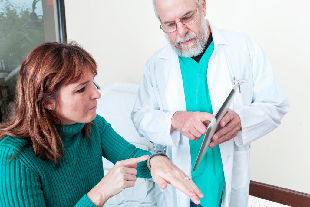 A male medical professional shows woman how to use health monitoring on tablet and smart watch.