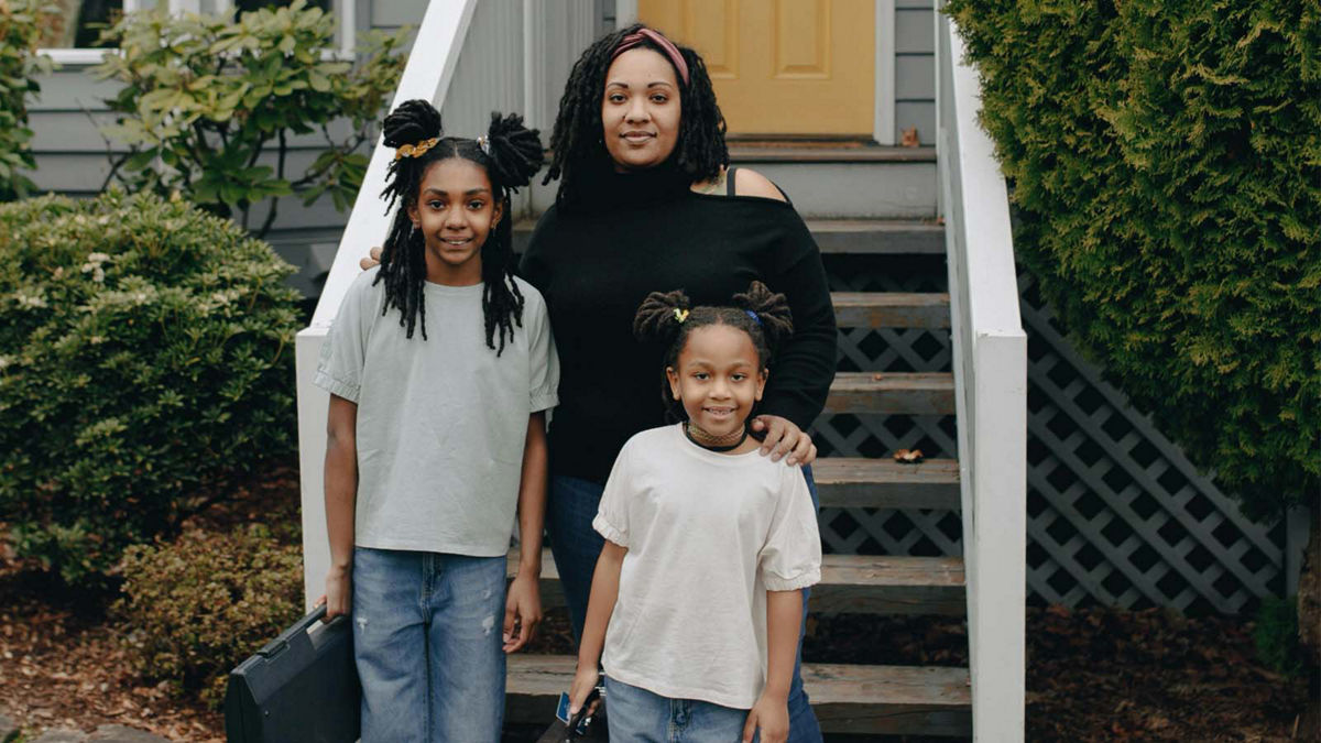 A mother and her two children stand in front of their front steps. 
