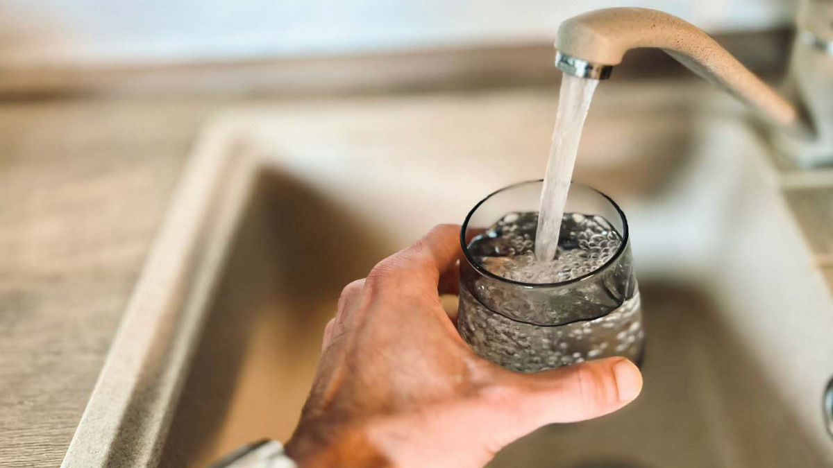 A person is holding a glass up to a kitchen faucet, filling it with water.