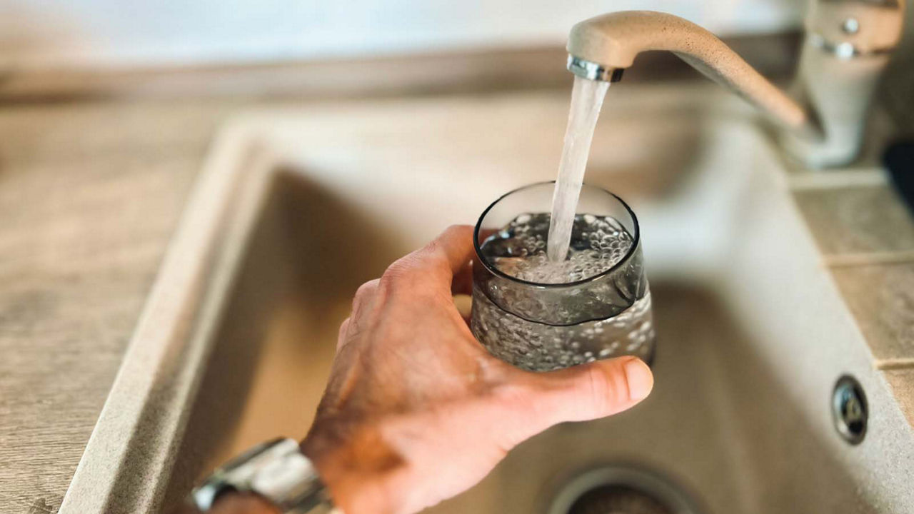A person is holding a glass up to a kitchen faucet, filling it with water.