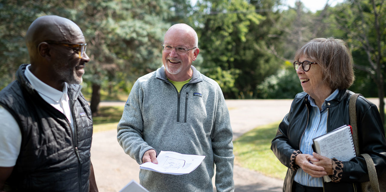Three people standing outside, two holding paperwork.