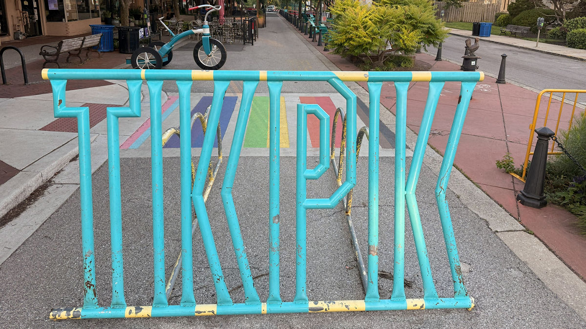 A metal "Takoma Park" sign in the middle of a sidewalk.