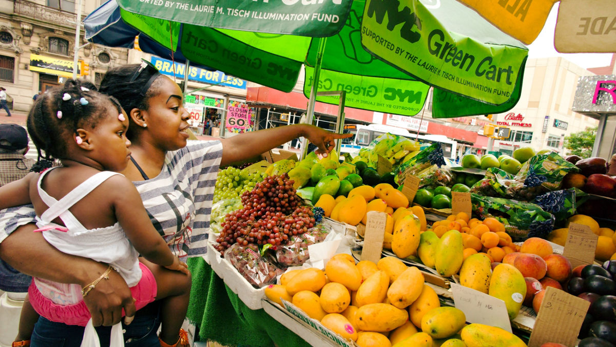 A woman and child choose fruits and vegetables from a fresh produce vendor.