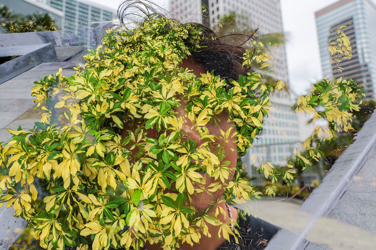 This double-exposure portrait blends a person with greenery and the city around them.