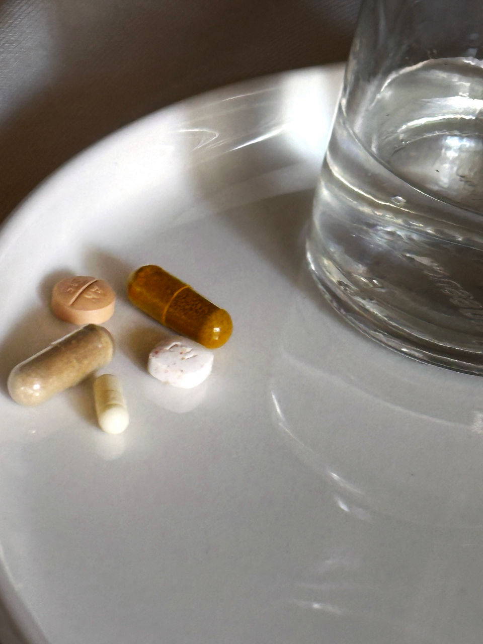 A glass of water next to a mundane-colored collection of pills.