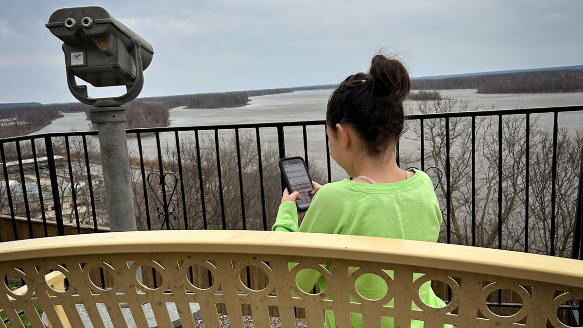 A teen is occupied with her cell phone on a bench near the bank of the Mississippi River in Burlington, Iowa.